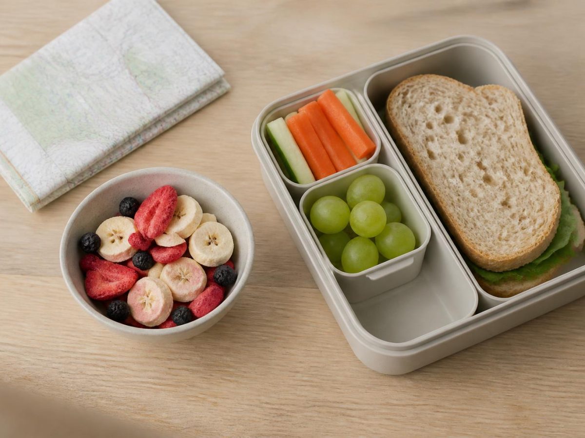 A lunchbox, a small bowl of freeze-dried fruit and a folded walking map laid out on a pale oak worktop